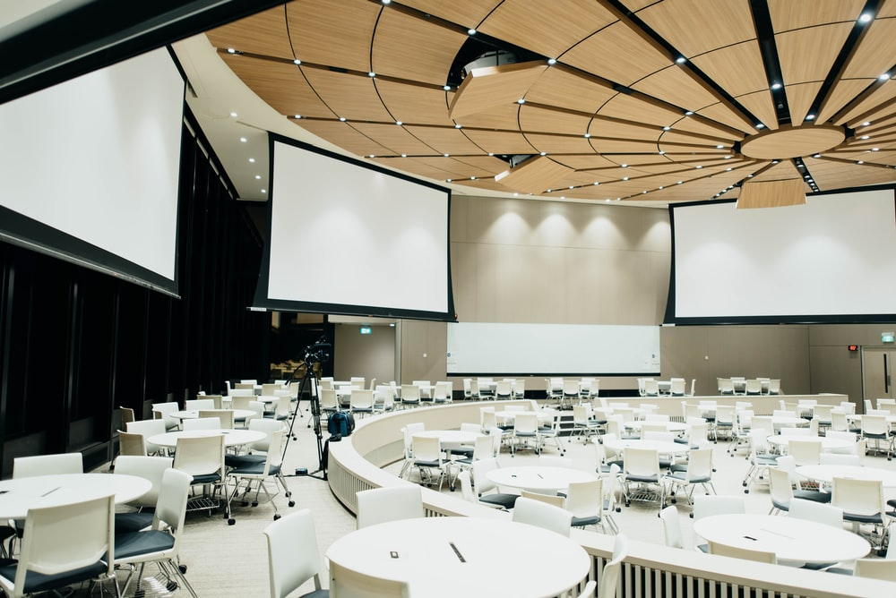 A Vacant Corporate Event Venue with Three Large Projector Screens and Several Tables and Chairs